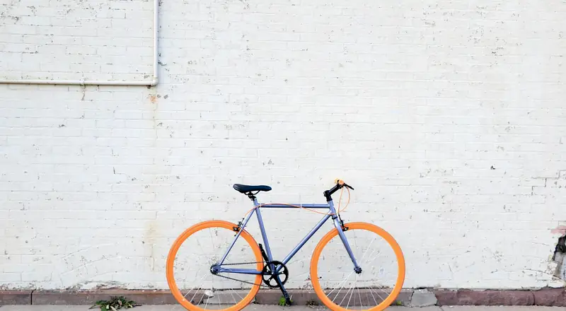 Bicicleta de rodas laranja diante de parede de tijolos